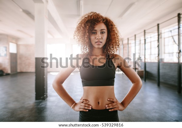 体育館に立ち 腰に手を当てたフィットな若いアフリカの女性のポートレート カメラにポーズを設定するフィットネスモデル の写真素材 今すぐ編集