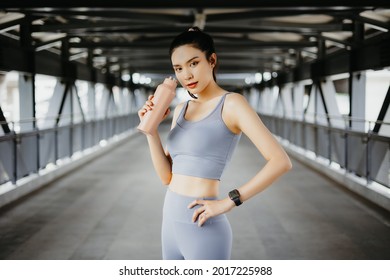 Portrait of fit young asian lady holding water bottle. Female runner taking a break after running workout. Healthy lifestyle and sport concepts. workout outdoors, wearing sports outfit.