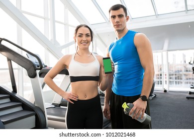 Portrait of fit young couple wearing sports clothes presenting mobile app holding smartphone with green screen and looking at camera - Powered by Shutterstock