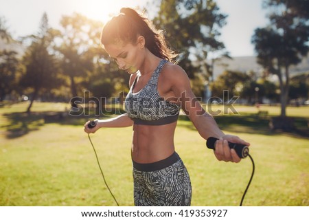 Portrait of fit young woman with jump rope in a park. Fitness female doing skipping workout outdoors on a sunny day.