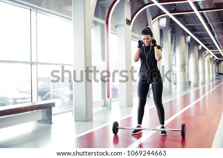portrait of fit young woman standing listening music at gym with barbells on floor