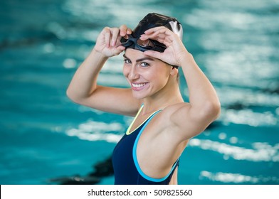 Portrait Of Fit Young Woman Wearing Swimming Cap And Goggles At The Pool. Portrait Of A Smiling Female Swimmer Wearing Swim Goggles At Swimming Pool. Happy Fit Girl At Pool Looking At Camera.