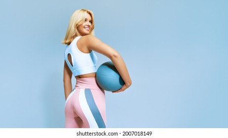 Portrait of a fitness happy fit woman standing holding a medicine ball. Copy Free space for text. Slim caucasian cross fit woman with fitness ball stand in gym, look. Plain light wall background - Shutterstock ID 2007018149