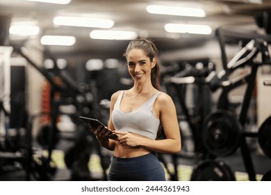 Portrait of a fitness instructor standing in a gym with tablet in her hands and smiling at the camera. - Powered by Shutterstock