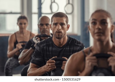 Portrait of fitness man lifting kettle bell with young women in fitness center. Active guy with group of people in gym doing weight lifting with kettlebell. Determined people in a row squatting. - Powered by Shutterstock