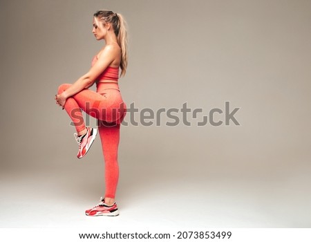 Portrait of fitness woman in pink sports clothing. Young beautiful model with perfect body.Female posing on grey background in studio.Cheerful and happy. Stretching out before training