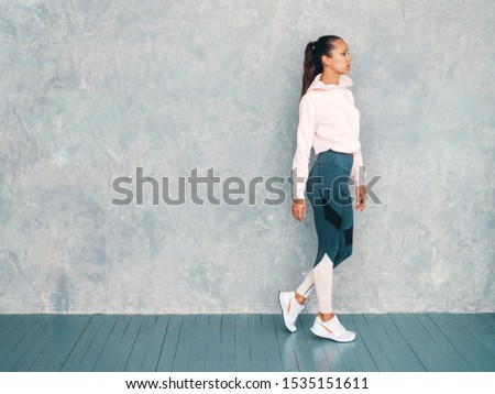 Portrait of fitness woman in sports clothing looking confident.Young female wearing sportswear. Beautiful model with perfect tanned body.Female posing in studio near gray wall