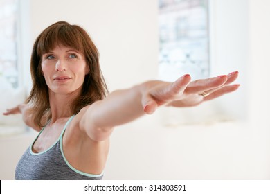 Portrait of fitness woman stretching her hands and looking away. Attractive mature woman exercising yoga in Virabhadrasana  pose. Female doing warrior pose in gym.