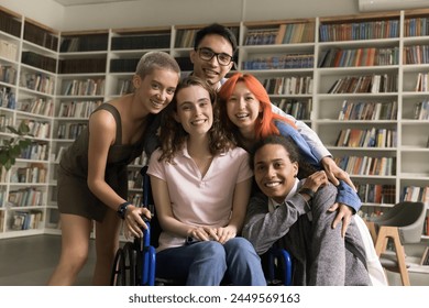 Portrait of five diverse schoolmates in library. Girl with physical disability sit in wheelchair posing for cam surrounded by friendly schoolmates, smile, express warm relation. Equality, friendship - Powered by Shutterstock