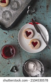 Portrait Flat Lay Image Of Linzer Cookies. Jam Filled Heart Shaped Biscuits On A White Round Plate. Baking Tools And Equipment Include Jam, Tray, Cutter And Icing Sugar. Love And Romance Food Concept