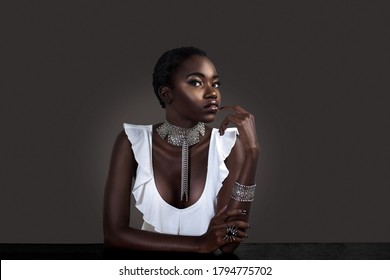 A Portrait Of A Flirtatious Young Black Female With Short Black Hair, Moist Lips, Perfectly Manicured Nails Wearing A White Sleeveless Blouse With Silver Jewelry Sitting At The Bar.