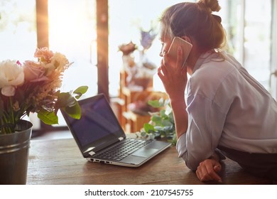 Portrait of florist in apron working at her own flower shop, using laptop and calling on the smart phone. She is leaning on wooden counter. She is arranging logistics, and delivery, taking orders - Powered by Shutterstock