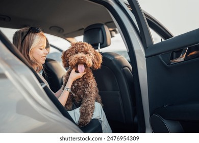 Portrait Fluffy brown Maltipoo dog with smiling little girl portrait while they sitting in back seat during car journey. Funny pets in a modern family concept. - Powered by Shutterstock