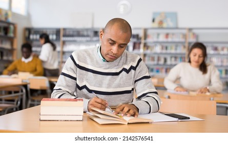 Portrait of focused adult latin american student studying in university library, making notes