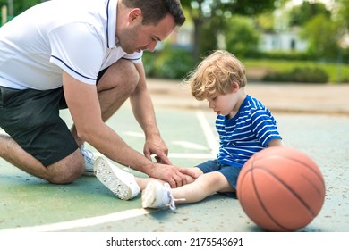 A portrait of focused adult man coach helping boy with knee trauma after playing basketball on the court - Shutterstock ID 2175543691