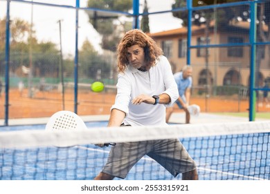 Portrait of focused adult man playing paddle tennis couple match at outdoors court - Powered by Shutterstock