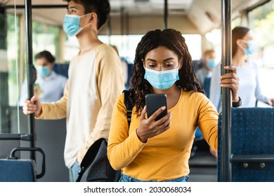 Portrait Of Focused African American Woman In Medical Face Mask Traveling On Public Transit And Using Cellphone, Standing And Holding Handle, Reading Sms Message, Chatting Online During Trip Ride