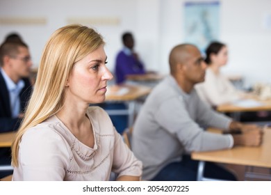 Portrait Of Focused Blonde Listening To Lecture In Classroom With Group Of Adult People. Postgraduate Education Concept