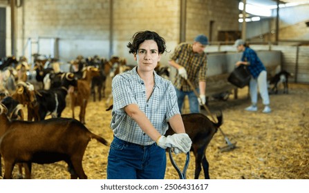 Portrait of focused busy Latin female employee working with hay and straw in barn on goat livestock farm - Powered by Shutterstock