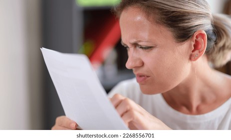 Portrait of focused female trying read text, squinting to see more clearly. Female having difficulties seeing text because of vision problems