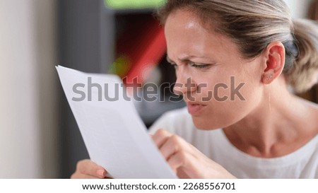 Portrait of focused female trying read text, squinting to see more clearly. Female having difficulties seeing text because of vision problems