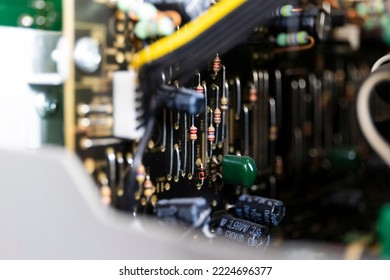 A portrait focused on a bunch of resistors on a black electronics print or circuit board in an open device in between other soldered components like capacitors. - Shutterstock ID 2224696377