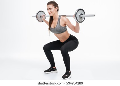 Portrait of a focused smiling fitness woman doing squats with barbell isolated on a white background