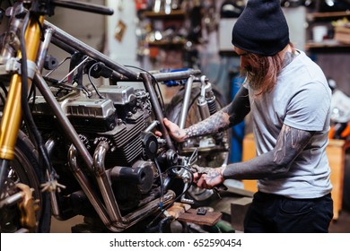 Portrait of focused tattooed man working in garage customizing  motorcycle and repairing broken parts - Shutterstock ID 652590454