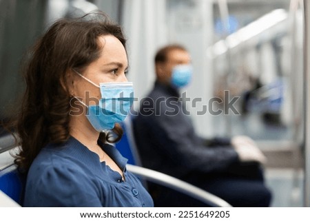 Portrait of focused woman in disposable mask and gloves traveling in subway train during daily commute to work in spring day. Concept of new life reality and precautions in COVID 19 pandemic