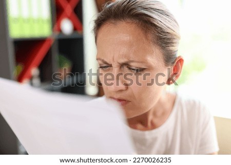 Portrait of focused woman trying read papers, squinting to see more clearly. Female having difficulties seeing text because of vision problems