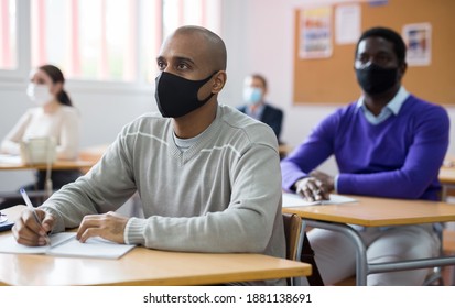 Portrait Of Focused Young Adult Male In Face Mask For Viral Protection Studying In Classroom With Colleagues