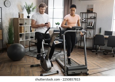 Portrait of focused young caucasian male and african female wearing sportswear using exercise bike and treadmill with phones looking online class how to lose weight. - Powered by Shutterstock