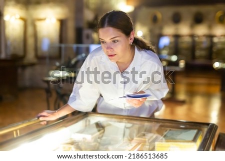 Portrait of focused young girl holding information booklet during visiting exposition of ancient boxes at museum