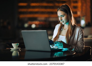 Portrait of a focused young remote worker sitting in a dark coffee shop and using high-tech gadgets for work. A young freelancer is using cutting-edge technologies.