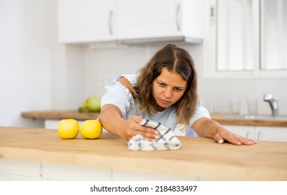 Portrait Of Focused Young Woman Cleaning Table With Cloth At Kitchen. Everyday Household Chores Concept