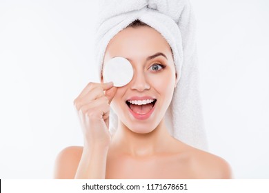 Portrait Of Foolish Playful Woman Using Sponge For Application Of Lotion Close One Eye With Cotton Keeping Open Mouth With Towel On Head Isolated On White Background