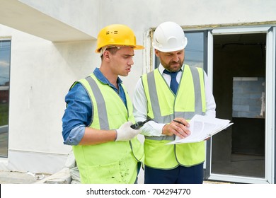 Portrait of foreman and supervisor discussing construction documents on site, both wearing hardhats and reflective vests