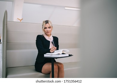 Portrait Of Formally Dressed Female Employee Working In Modern Office Interior Sitting At Table With Education Literature, Attractive 30 Years Old Woman Posing Spending Time For Planning Startup