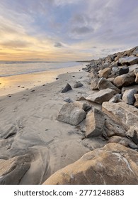 Portrait format view looking down the line of a rocky riprap breakwater protecting the Carlsbad coast.