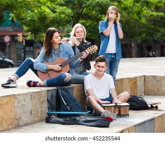 Portrait Of Four Smiling European  Teenagers Playing Music Together Outdoors  