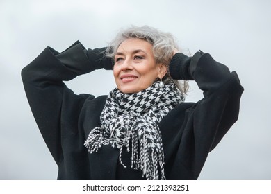 Portrait of a free, independent and happy mature woman in warm clothes against a gray autumn sky