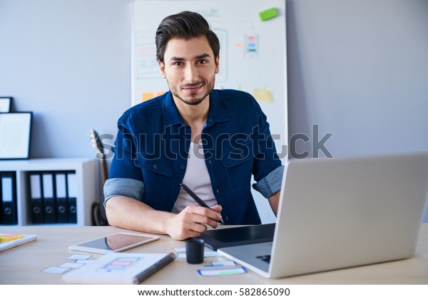 Portrait of freelance graphic designer sitting at\
desk with laptop and\
tablet