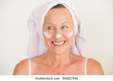 Portrait Friendly Attractive Mature Woman With Towel And Protective Skin Care Creme And Moisturizer Lotion On Happy Smiling Face, Bright Background.