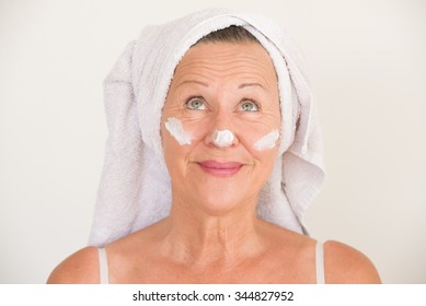 Portrait Friendly Attractive Mature Woman With Towel And Protective Skin Care Creme And Moisturizer Lotion On Happy Smiling Face, Bright Background.