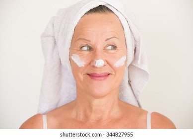 Portrait Friendly Attractive Mature Woman With Towel And Protective Skin Care Creme And Moisturizer Lotion On Happy Smiling Face, Bright Background.