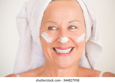 Portrait Friendly Attractive Mature Woman With Towel And Protective Skin Care Creme And Moisturizer Lotion On Happy Smiling Face, Bright Background.