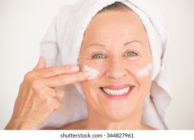 Portrait Friendly Attractive Mature Woman With Towel And Protective Skin Care Creme And Moisturizer Lotion On Happy Smiling Face, Bright Background.