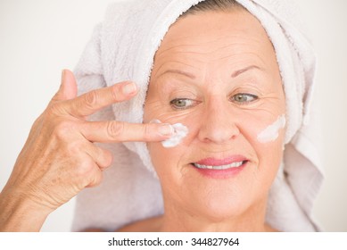 Portrait Friendly Attractive Mature Woman With Towel And Protective Skin Care Creme And Moisturizer Lotion On Happy Smiling Face, Bright Background.