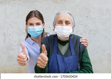 Porträt einer freundlichen Betreuerin, die sich mit einer älteren kranken Frau, die wegen einer Covid-19-Pandemie eine chirurgische Maske trägt, posiert und die Daumen nach oben zeigt