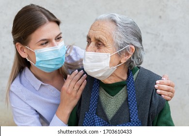 Porträt einer freundlichen Betreuerin, die sich mit einer älteren kranken Frau ausstellt, die wegen einer Covid-19-Pandemie eine chirurgische Maske trägt